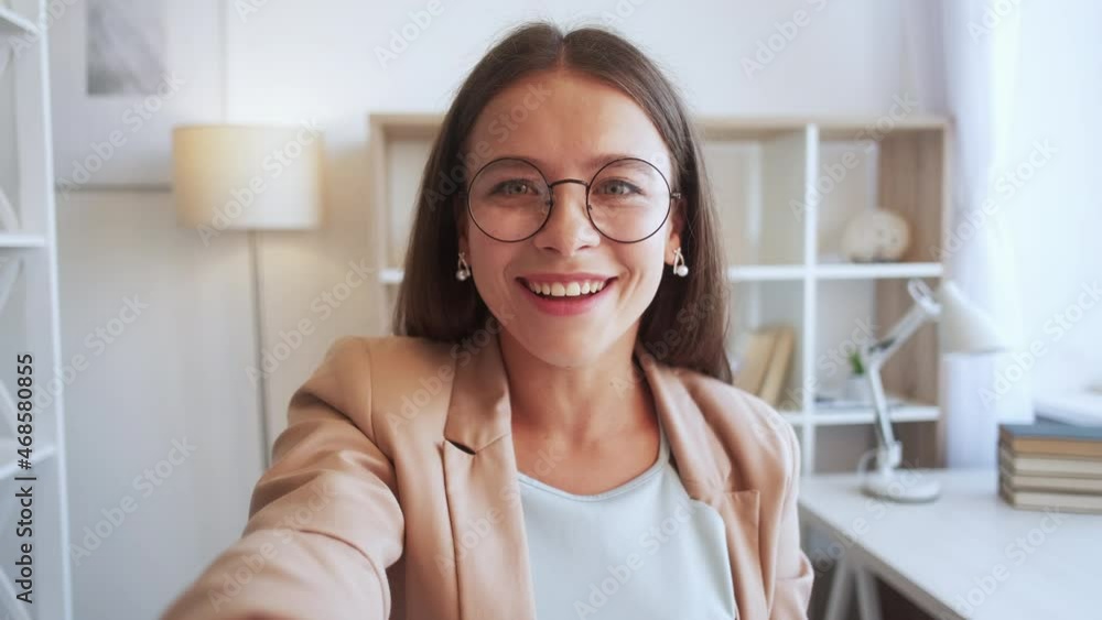 Video call. Excited woman. Distance communication. Happy smart lady in spectacles talking on camera with friends in light room interior. Video call. Excited woman. Distance communication. Happy smart lady in spectacles talking on camera with friends in light room interior.