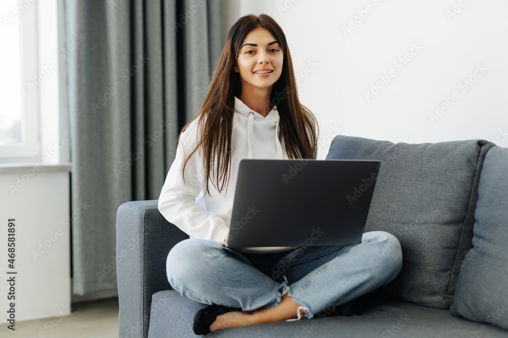 Young woman doing research work for her business. Smiling woman sitting on sofa relaxing while browsing online shopping website. Young woman doing research work for her business. Smiling woman sitting on sofa relaxing while browsing online shopping website.