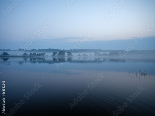 misty morning by the lake with calm water  fog and reflections of trees in mirror