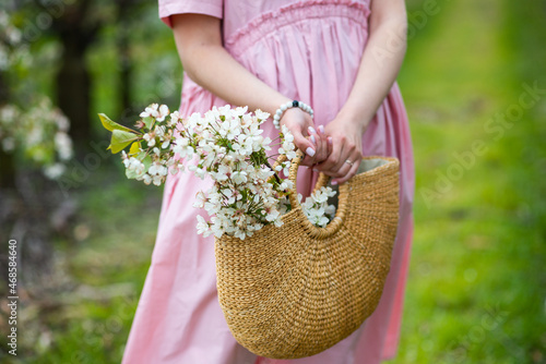 Caucasian Female in pink dress holds hand made basket full of white spring blooming flowers