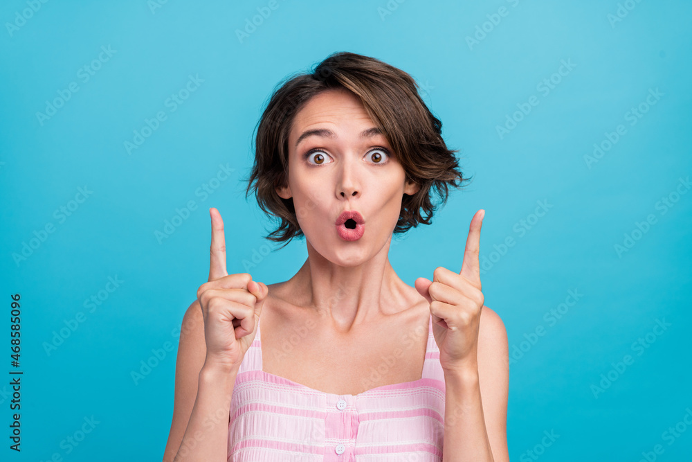 Photo of impressed young shop assistant lady point index up wear pink top isolated on blue color background Photo of impressed young shop assistant lady point index up wear pink top isolated on blue color background