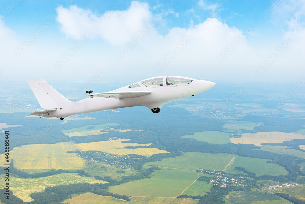 Glider flying high in the sky over fields and forests, aerial view.