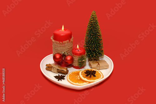 White plate with a red candle and dried oranges and a pine cone. Mini tree.