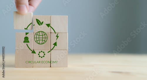 Circular economy concept, recycle, environment, reuse, manufacturing, waste, consumer, resource. Sustainable development. Hand put wooden cubes; the symbols of circular economy on grey background. photo