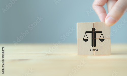 Business ethics concept. Business moral principles concept. Hand holds the wooden cubes with "ETHICS" symbols on grey background and copy space. Banner for business integrity, good governance policy.