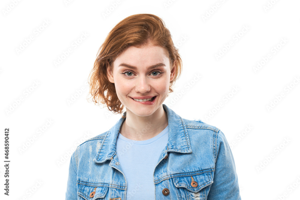 A student with red hair thinks happily, bites her lip and looks straight. Pensive woman in a blue denim jacket on a white background. Copy space A student with red hair thinks happily, bites her lip and looks straight. Pensive woman in a blue denim jacket on a white background. Copy space