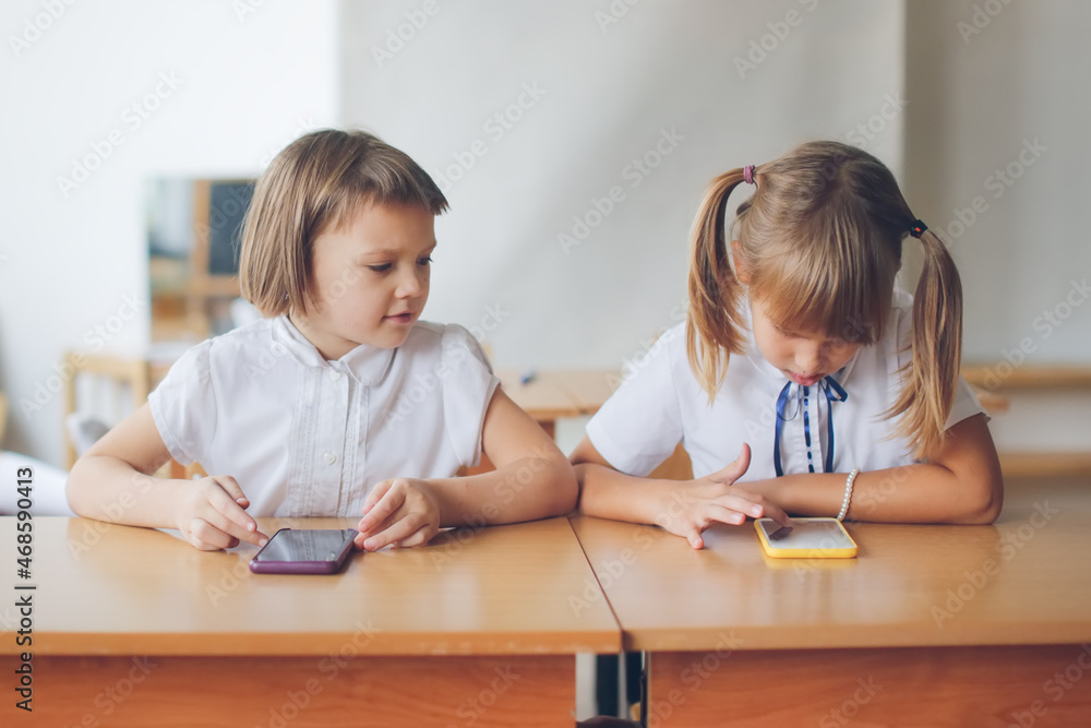 Girls friends schoolgirls desk with telephones, schoolchildren and gadgets, digital addiction at school,attention deficit disorder, clip thinking. Communication problems classmates with smart phones Girls friends schoolgirls desk with telephones, schoolchildren and gadgets, digital addiction at school,attention deficit disorder, clip thinking. Communication problems classmates with smart phones