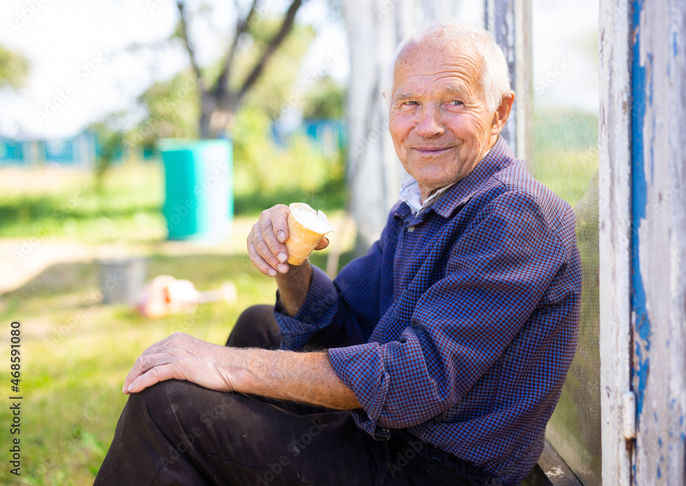 elderly man eating creamy ice cream in waffle cup near greenhouse in village garden elderly man eating creamy ice cream in waffle cup near greenhouse in village garden