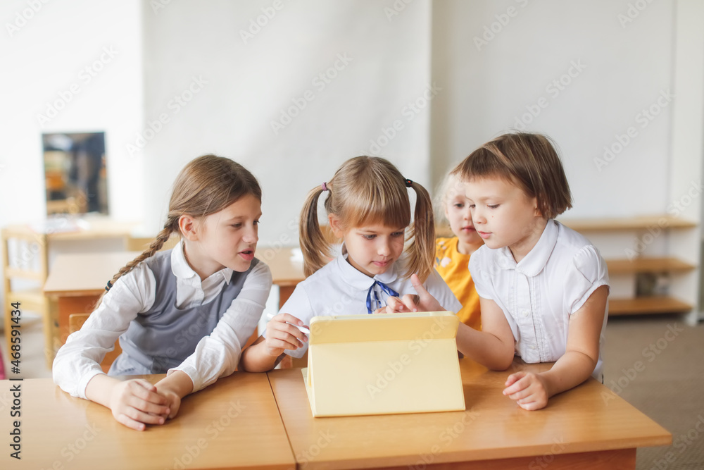 Three children of classmates at school work together with a digital tablet, gadgets in class and in education. Three girls look and draw on the tablet at a desk, modern education and technology Three children of classmates at school work together with a digital tablet, gadgets in class and in education. Three girls look and draw on the tablet at a desk, modern education and technology