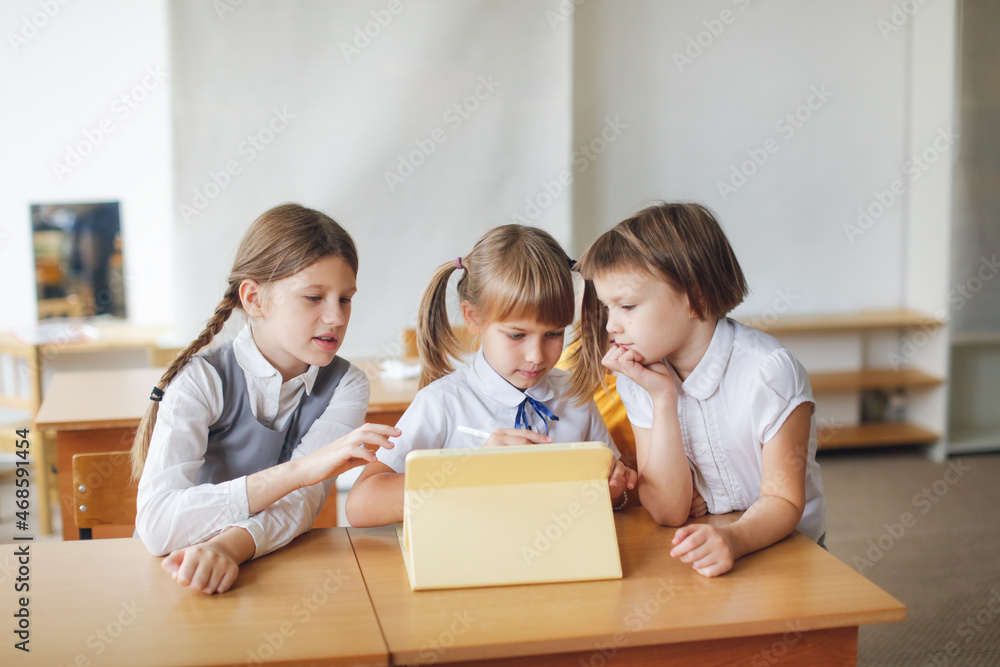 Three children of classmates at school work together with a digital tablet, gadgets in class and in education. Three girls look and draw on the tablet at a desk, modern education and technology Three children of classmates at school work together with a digital tablet, gadgets in class and in education. Three girls look and draw on the tablet at a desk, modern education and technology