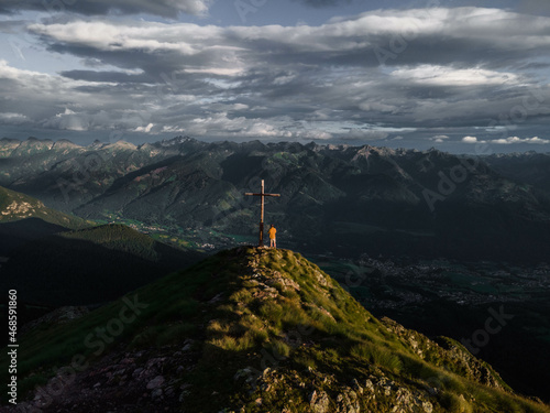 Mann an einem Gipfelkreuz in den Alpen. Südtirol im Herbst / Sommer. 