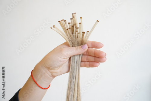 Natural Hair extensions blonde woman.  Keratin capsules of blonde hair extensions in the hand on white background