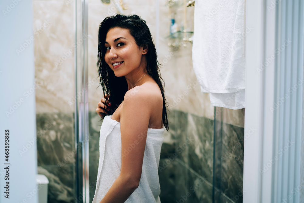 Half length portrait of charming Asian woman in white towel smiling at camera after showering in hotel bathroom, happy female model posing during morning time for bathing and relaxing indoors Half length portrait of charming Asian woman in white towel smiling at camera after showering in hotel bathroom, happy female model posing during morning time for bathing and relaxing indoors