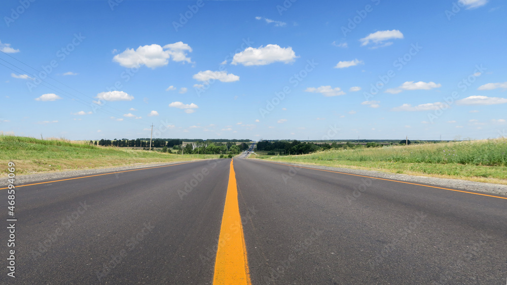 New asphalt pavement on the background of green fields to the horizon. A straight highway with a yellow flat strip on the background of a rural landscape