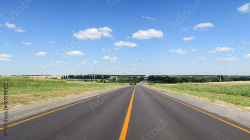 New asphalt pavement on the background of green fields to the horizon. A straight highway with a yellow flat strip on the background of a rural landscape