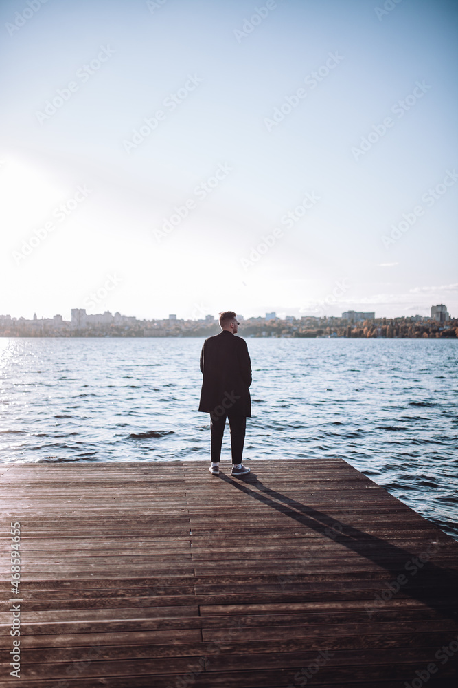 a young guy with a beard looks melancholically at the view of the lake