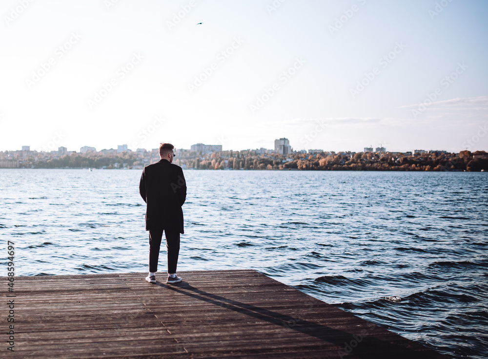 a young guy with a beard looks melancholically at the view of the lake