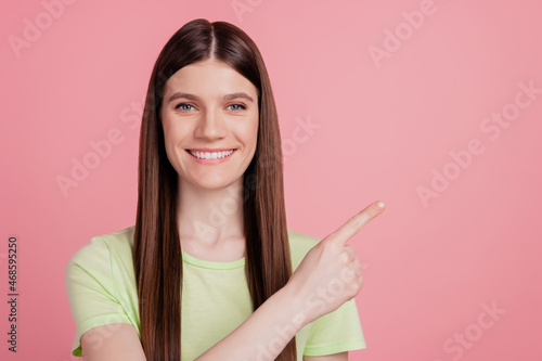 Portrait of young charming attractive cheerful girl pointing finger empty space select suggest sale isolated over pink background