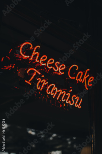 Neon sign phrase ' Tiramisu and Cheesecake '. Bright glowing red neon sign in cafe interior
