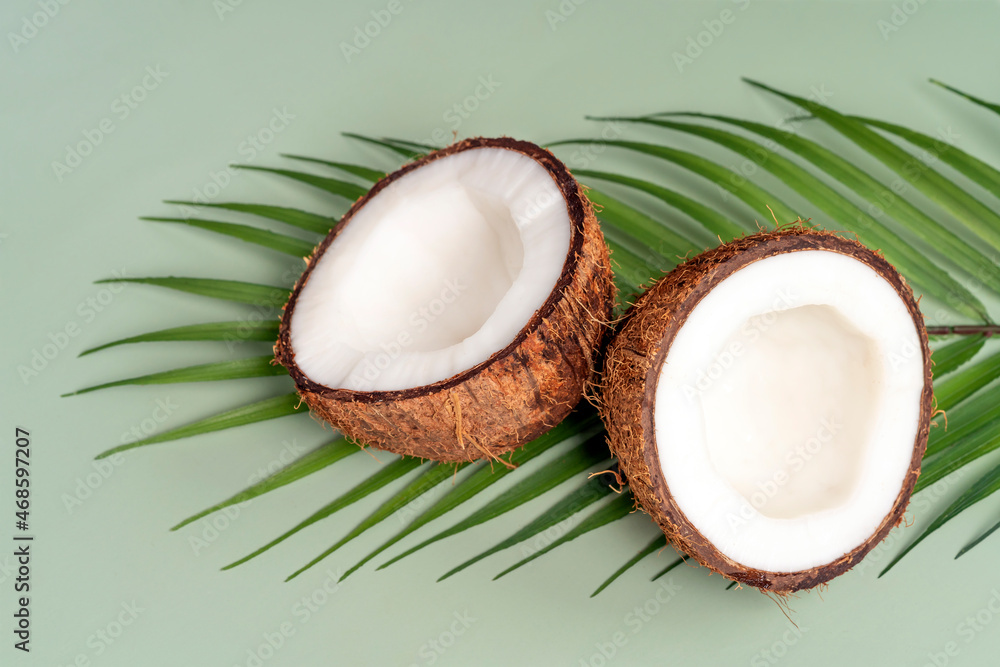 Coconut halfs, tropical leaf on green background. Close-up. Spa, organic cosmetics concept. Coconut halfs, tropical leaf on green background. Close-up. Spa, organic cosmetics concept.