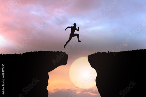 silhouette of businessman jumping over the cliff on sunset background, business concept idea photo