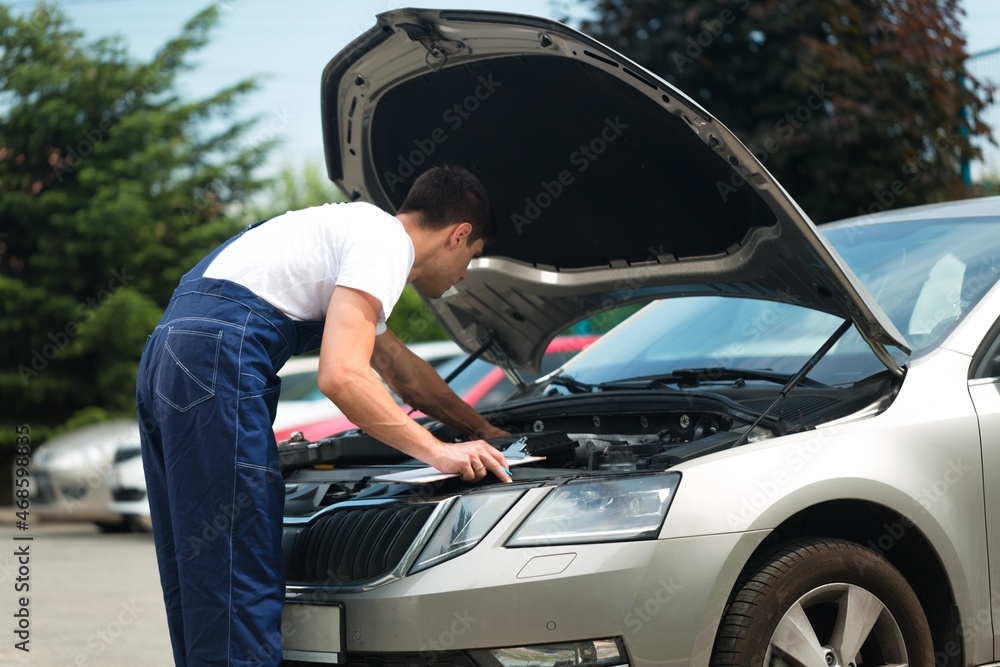 Mechanic writing job checklist to the clipboard at a workshop with a car Mechanic writing job checklist to the clipboard at a workshop with a car