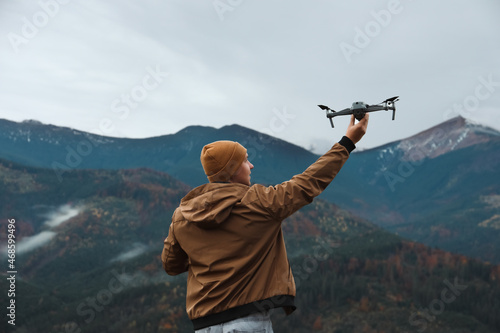 Young man with modern drone in mountains, back view photo
