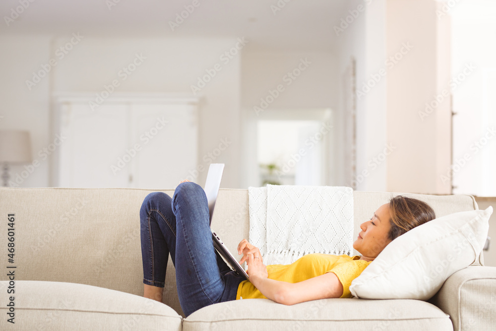 Happy asian woman lying on sofa, resting with laptop at home Happy asian woman lying on sofa, resting with laptop at home