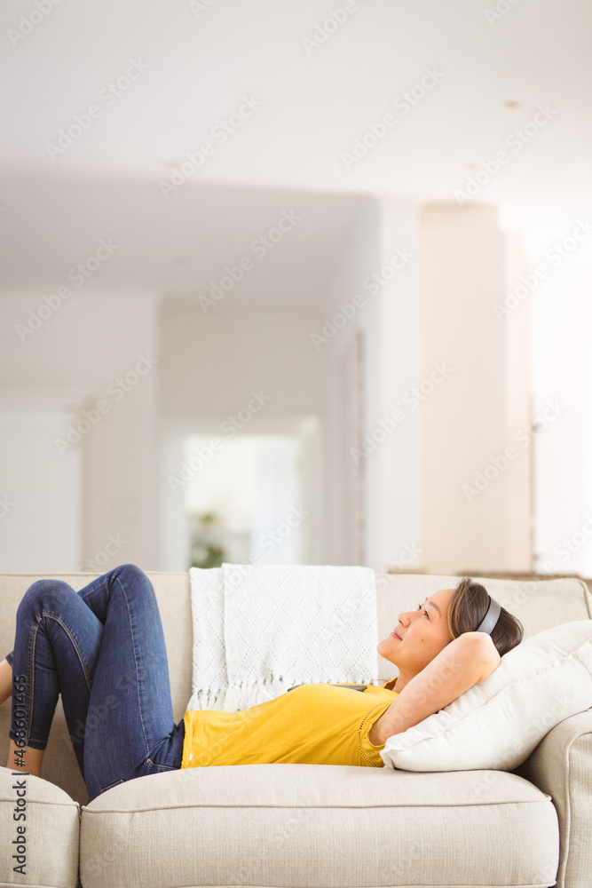 Happy asian woman wearing headphones resting on sofa at home Happy asian woman wearing headphones resting on sofa at home