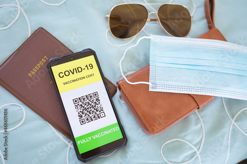 Glasses, face mask, documents and smartphone with covid 19 passport on screen lying on bed