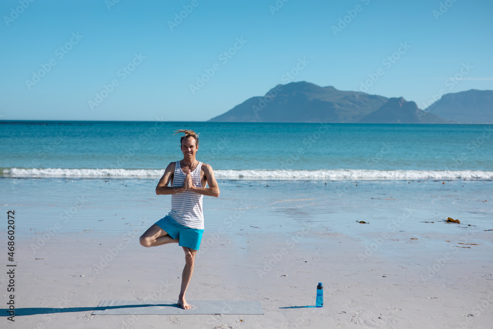 Man practicing tree pose yoga posture at beach against clear blue sky with copy space Man practicing tree pose yoga posture at beach against clear blue sky with copy space