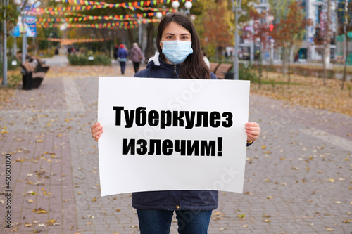 A masked woman holds a poster with text in Russian, translated from Russian - Tuberculosis is curable photo