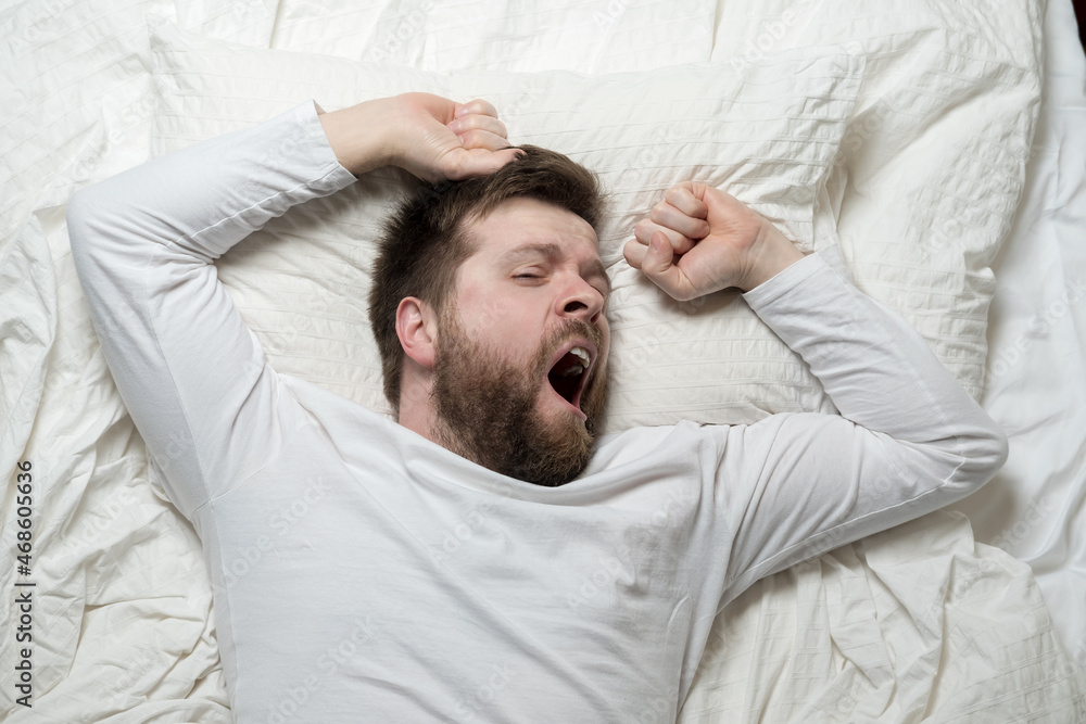 Cute bearded man wakes up from sleep, he yawns and stretches as he lies in bed. Top view. Close-up. Cute bearded man wakes up from sleep, he yawns and stretches as he lies in bed. Top view. Close-up.