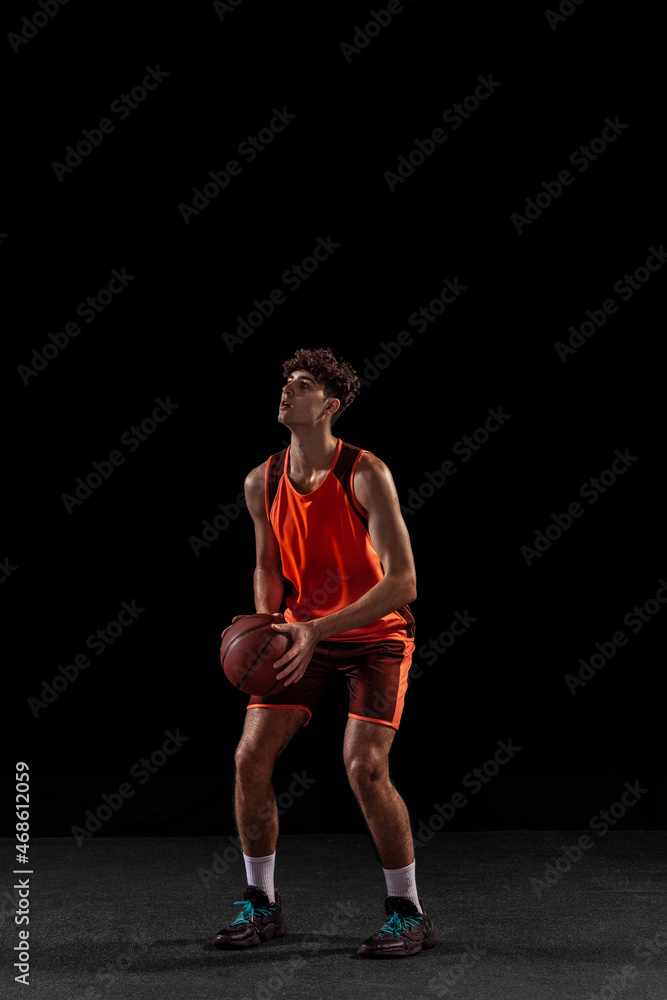 Full length portrait of basketball player training isolated on dark studio background. Tall muscular athlete jumping with ball. Full length portrait of basketball player training isolated on dark studio background. Tall muscular athlete jumping with ball.