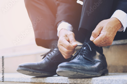 Close up of businessman hand tie shoelaces wearing leather shoes sitting on staircase background.