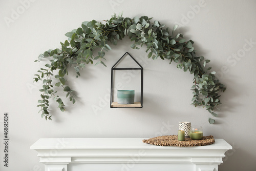Beautiful garland made of eucalyptus branches and aromatic candle hanging above mantelpiece indoors photo