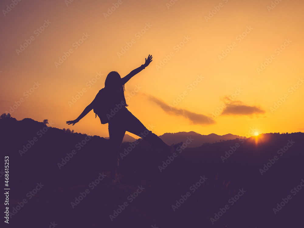 Silhouette of happy woman with open arms on peak of mountain at sunset.