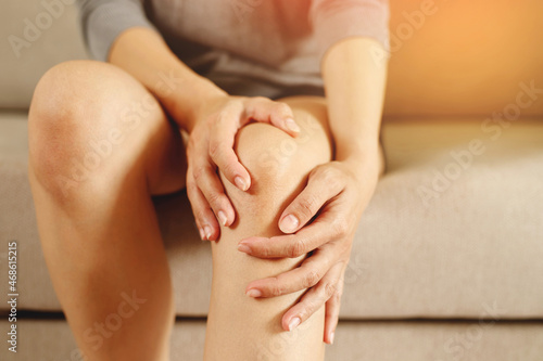 A woman suffering from feeling knee pain sitting sofa at home. hand massaging his painful knee. Health care and medical concept.