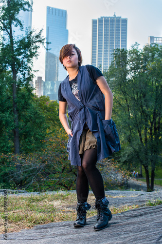 Dressing in a blue sleeveless long blouse, black leggings and boots, two hands putting in pockets, hair covering one eye, a young Chinese girl is standing in a small words.