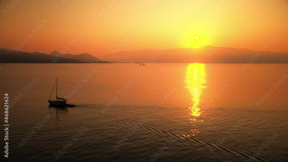 Sunset on the Ionian Sea coast, Greece. Bright Sun, land in the distance, floating boats, reflections in the water Sunset on the Ionian Sea coast, Greece. Bright Sun, land in the distance, floating boats, reflections in the water