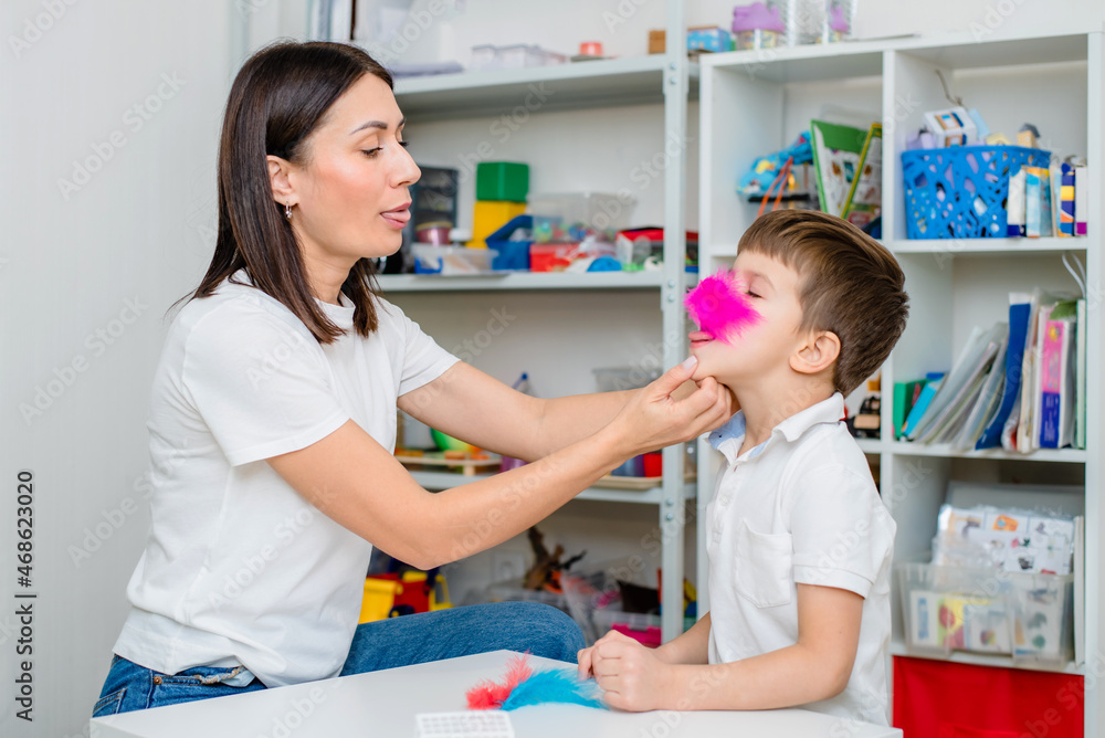 Woman speech therapist training boy to blow correctly using colored feathers exercise
