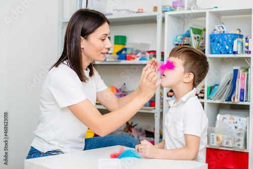 A woman speech therapist teaches a child to blow correctly on colored feathers.