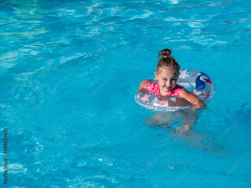 Smiling little girl with colorful inflatable ring in the pool with blue water.