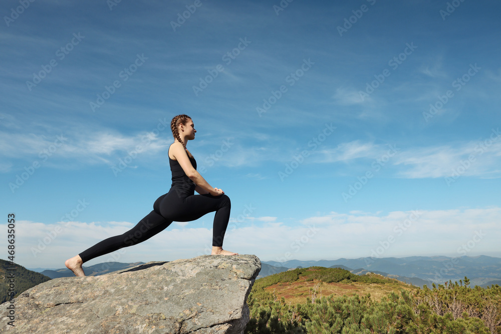Beautiful young woman stretching on rock in mountains Beautiful young woman stretching on rock in mountains