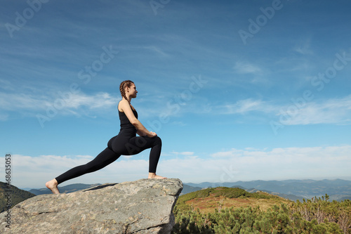 Beautiful young woman stretching on rock in mountains