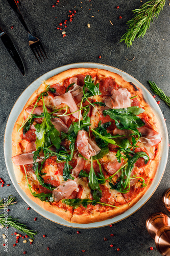 pizza with ham, salami and arugula on a dark background. top view