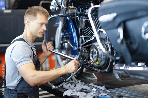Male car mechanic holds wrench and looks at open motorcycle engine