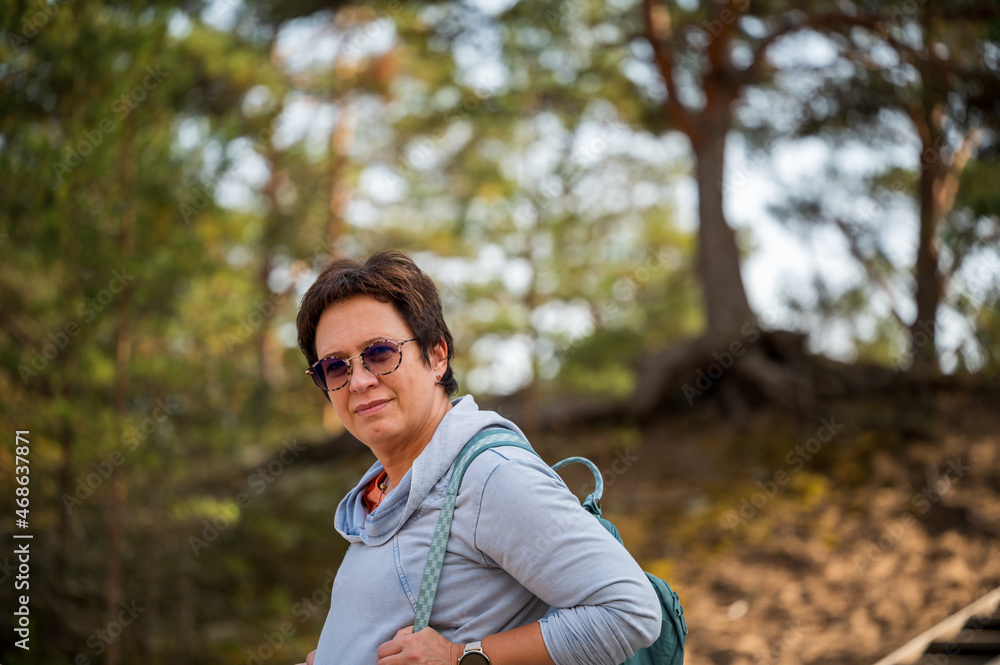 A 50-year-old woman with a sporty lifestyle. Portrait of smiling mature woman who sports and hikes in nature. Woman with a backpack hiking in the woods. The concept of recreation.