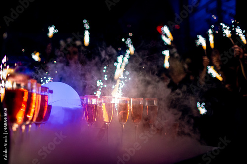 A lot of champagne flutes on banquet table with sparklers in nightclub, limited focus depth