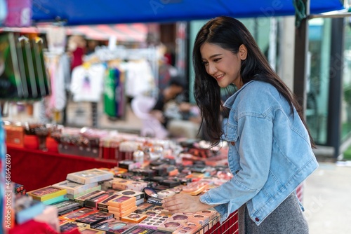 Beautiful asian female young model lady having a solo shopping and stroll walk time by herself and looking through concentratedly some fashion dresses put on sale at a fashion store in a night market 